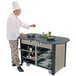 A chef standing next to a Lakeside stainless steel cooking cart with food on it.