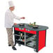 A chef standing next to a Lakeside stainless steel induction cooking cart with red laminate finish.