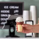 A hand holding a JOY chocolate dipped flat bottom cake cone filled with ice cream.