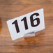An American Metalcraft hammered aluminum cylinder table card holder with a white sign and black numbers on it.