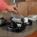 A hand using a Vollrath Lidsaver to dispense a plastic lid over a bowl on a counter.