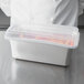 A chef in a white coat holding a Vollrath clear container with a clear lid.