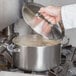 A hand using a Vollrath Miramar casserole pan with a low dome lid.