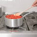 A person stirring red sauce in a Vollrath Wear-Ever sauce pan on a stove with a wooden spoon.