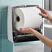 A large white hardwound paper towel roll being loaded into a wall-mounted dispenser.