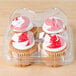 A plastic container with four cupcakes with red and white frosting.