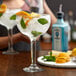 A woman pouring gin into a Libbey Super Stems cocktail glass filled with ice and mint.