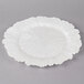 A white Charge It by Jay glass charger plate with a scalloped edge and a circular design.