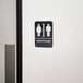 A Thunder Group black and white unisex restroom sign with Braille on a wall.