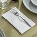 A fork and knife on a white linen-feel dinner napkin on a white plate.