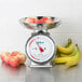 An Edlund stainless steel portion scale on a counter with apples and bananas in a bowl.