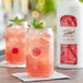 A glass of pink raspberry lemonade with mint leaves next to a white bottle of Torani Raspberry Puree Blend.