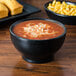 A black china bowl of chili on a table with cornbread.