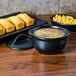 A Hall China black onion soup bowl filled with soup on a table with bread.