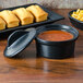 A black Hall China casserole dish on a wood surface filled with macaroni and cheese.