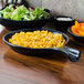 A black Hall China fry pan server with macaroni and salad on a table.