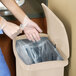 A woman in a scrub suit and gloves stepping on a Rubbermaid Slim Jim trash can.