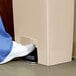 A person in white shoes stepping on the front pedal of a Rubbermaid Slim Jim rectangular trash can.