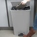 A woman using her foot to open a Rubbermaid Slim Jim trash can.