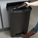 A woman using a Rubbermaid Slim Jim black front step-on trash can to throw away garbage.