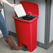 A woman using the red Rubbermaid Slim Jim trash can to throw away a book.