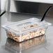 A Carlisle clear plastic container lid with food in it on a counter with a spoon notch.