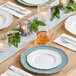 A table set with white plates, silverware, and a Choice white linen-feel dinner napkin with a fork and knife on top.