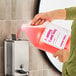 A gallon container of Advantage Chemicals foaming hand soap being poured into a wall-mounted soap dispenser.