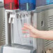 A person using a Crathco cold beverage dispenser to fill a plastic cup.