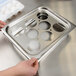 A person's hand holding a stainless steel tray with 8 holes in it.