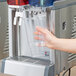 A hand filling a plastic cup with water from a Crathco cold beverage dispenser.
