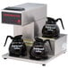 A Grindmaster commercial pourover coffee maker with three warmers, one on top and two on the bottom, and coffee pots on the warmers.