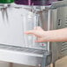 A person's hand holding a plastic cup under a Crathco beverage dispenser spout.