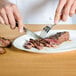 A person using a Victorinox serrated steak knife to cut a piece of meat on a plate.