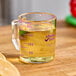 A purple Cambro polycarbonate measuring cup with yellow liquid and a lemon slice.