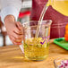 A person pouring liquid into a purple Cambro measuring cup.