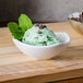 A white American Metalcraft sauce cup filled with mint chocolate chip ice cream and topped with mint leaves and chocolate chips.