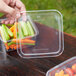 A hand holding a Fabri-Kal plastic container filled with vegetables.