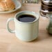 A Tuxton Yukon china mug filled with coffee on a table with a plate of bread.