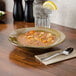A Tuxton Mojave china soup bowl filled with soup and a glass of water with a lemon wedge on a table.