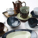 A Tuxton TuxTrendz Artisan Sagebrush saucer on a table with tea cups.