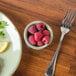 A TuxTrendz Sagebrush ramekin filled with raspberries on a table with a plate of food and a fork.