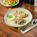 A Tuxton Artisan Sagebrush China plate with grilled chicken, rice, and a lemon wedge on a table.
