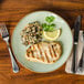 A Tuxton Artisan Sagebrush china plate with grilled chicken, rice, and vegetables with a lemon slice.