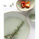 A close-up of a Tuxton Artisan Sagebrush china bowl with a sprig of rosemary and a red bell pepper.