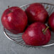 An oval stainless steel basket filled with red apples.