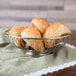 An American Metalcraft stainless steel oval basket filled with bread on a table.