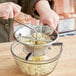 A person using a Tellier stainless steel food mill to press potatoes into a bowl.
