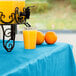 A glass of orange juice on a turquoise table with a drink dispenser and oranges.