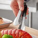 A person holding Vollrath stainless steel scalloped tongs with a black Kool-Touch handle over a tray of green food.